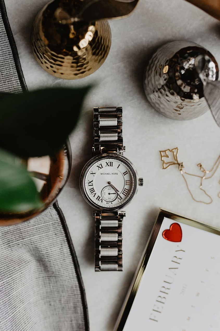 En elegant arrangerad samling av smycken, inklusive en Michael Kors-klocka, på en vit yta.